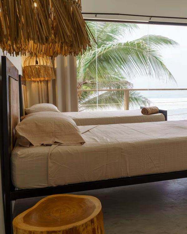 A guest room at La Ola, bed facing open doors onto a balcony with palms and ocean beyond