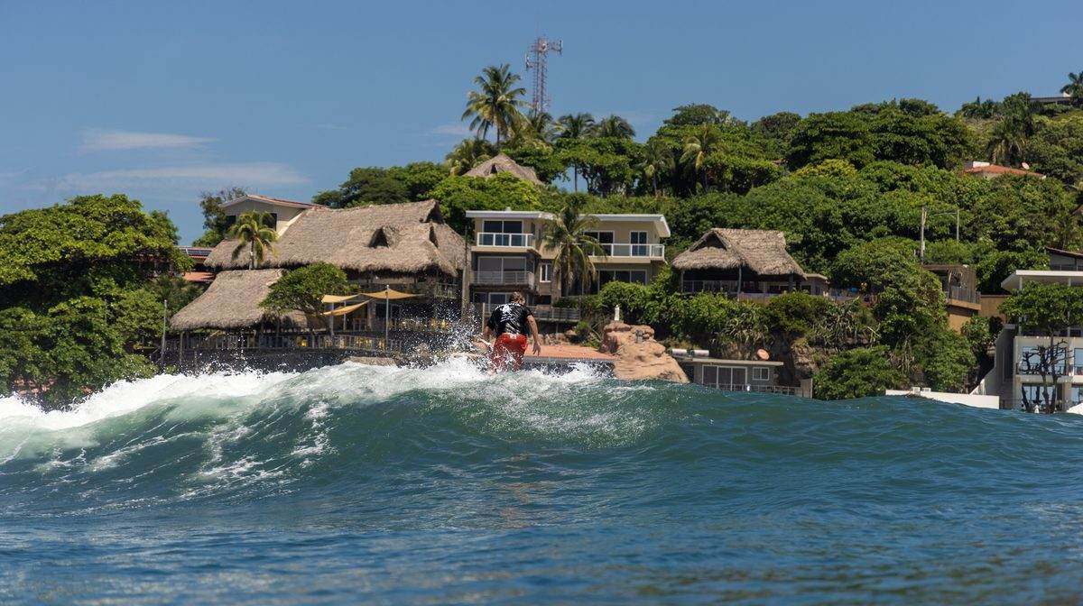 Kevin riding a wave at El Sunzal with the shoreline behind him