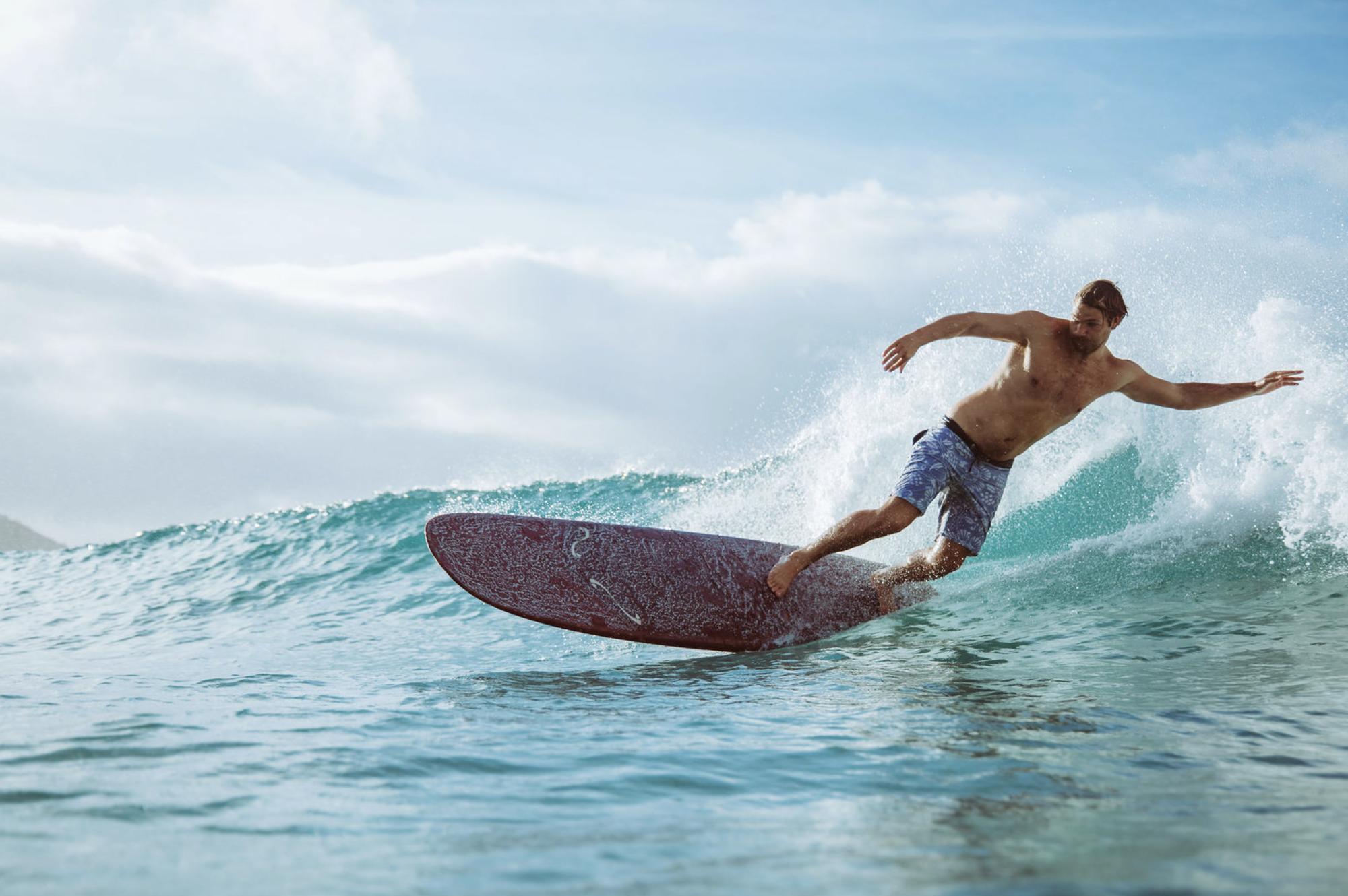 A longboarder carving a turn on a clear blue wave, spray coming off the rail
