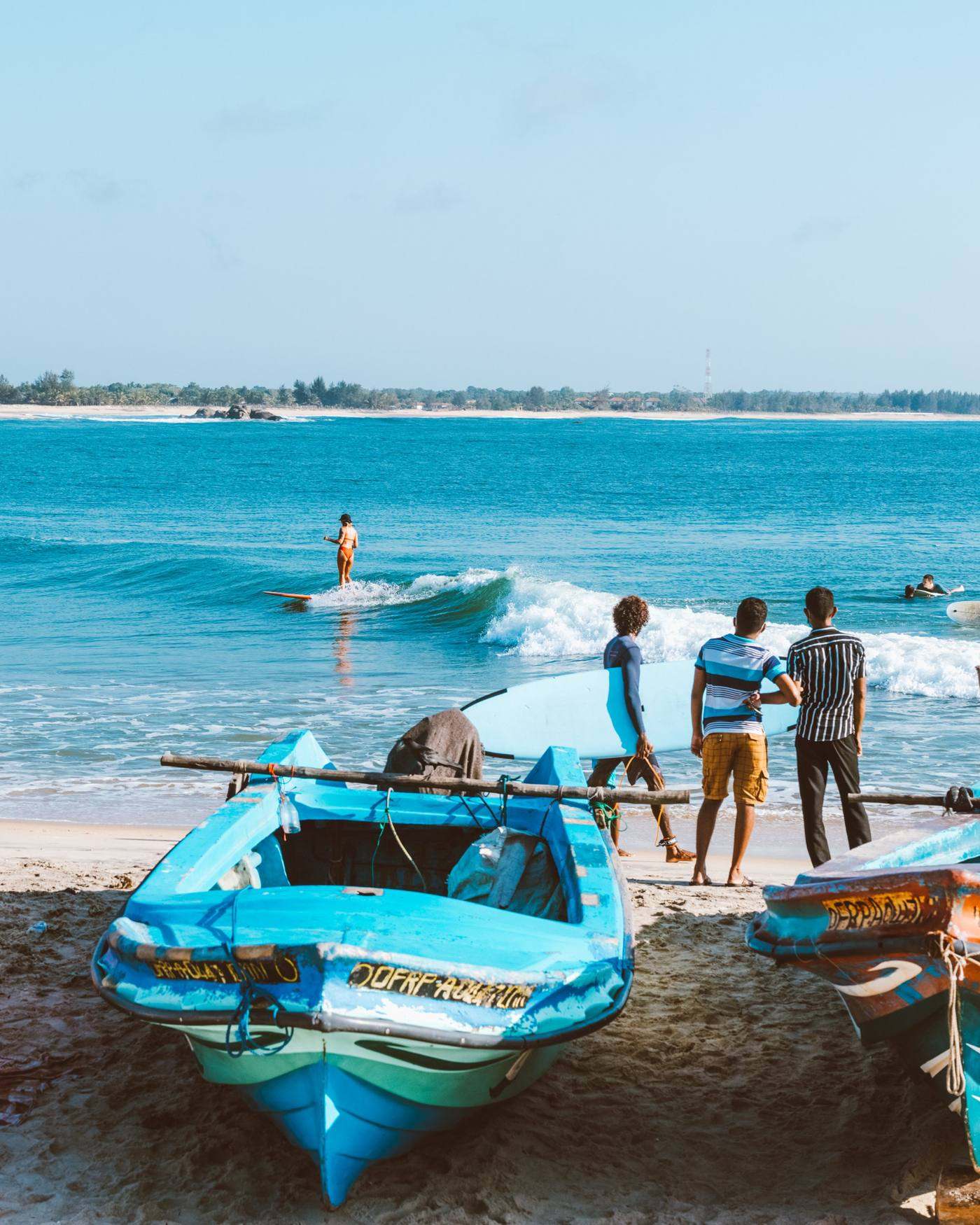A longboarder on a small right at Arugam Bay, fishing boats pulled up on the sand in front