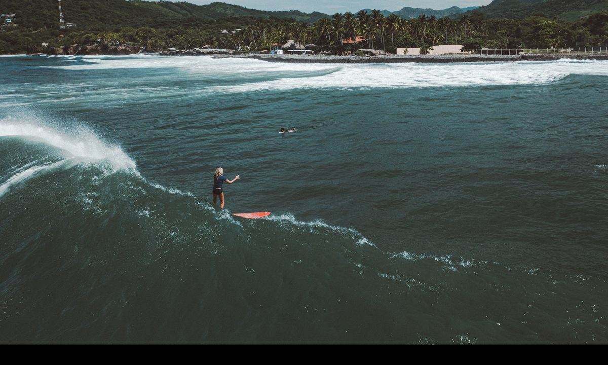 Drone view of a longboarder trimming down a long wall at El Sunzal with the town behind